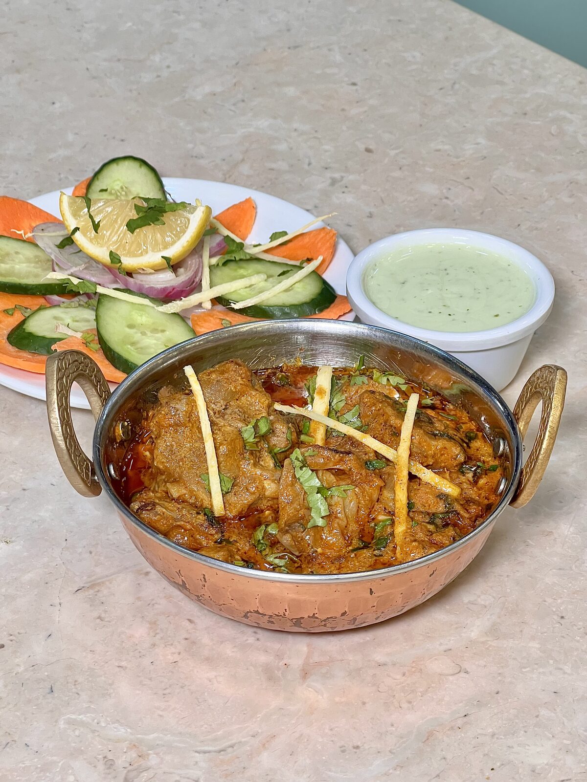 Beef Qorma served in a copper karahi with salad and raita